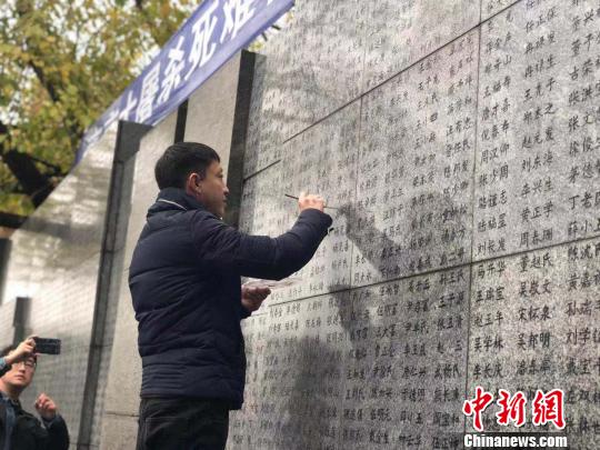10日晨，下着小雨。南京大屠杀幸存者、死难者遗属、学生们依次描写名字，祭悼南京大屠杀遇难同胞。淡淡的墨汁掺着雨水，渗入了刻在纪念馆灰色厚重石壁上的黑色名字中。　朱晓颖 摄