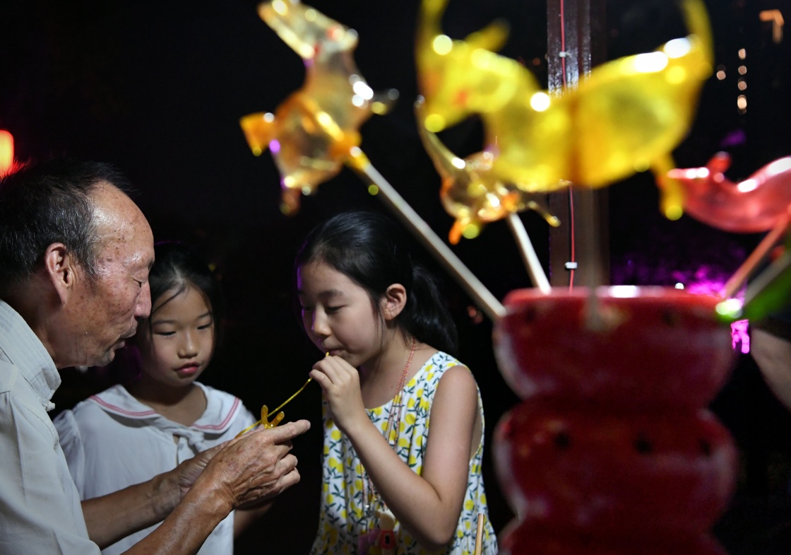 7月7日晚,小朋友在洛阳洛邑古城内吹糖人. 新华社记者 李安 摄
